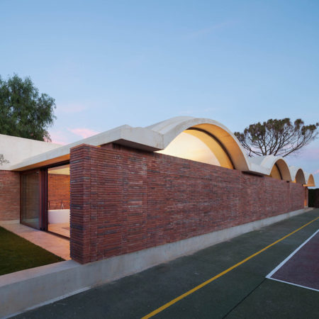 ELCHE, Spain — A project of three years, a home in Elche, Spain uses open brick spaces to extend leisurely areas into the hot, humid outdoor climate. The brick extension is the work of Barcelona-based Mesura architects. [caption id="attachment_30842" align="alignnone" width="1200"] Click to see a larger image.[/caption] [caption id="attachment_30843" align="alignnone" width="1181"] Click to see a larger image.[/caption] The studio says the new cross volume adds additional dimensions to the lawn, adding brick walls and arches to define space, atmosphere and a link between the home and the nearby pool. The studio told ArchDaily: It is located in the countryside around the city of Elche, in a hot and humid climate and barren landscape. The site consists of an existing home in the center of the field, leaving undefined surroundings: bad quality spaces and no exterior-interior relationship. The first intention will be to limit the exterior spaces through a new built volume generating a triangulation between this, the existing house and the pool. The intention is to separate the lived spaces of intimate spaces in relation to the climate, solar orientation, visual, topography and vegetation. [caption id="attachment_30844" align="alignnone" width="1200"] Click to see a larger image.[/caption] The extension increases the privacy of the home, while also extending the livable area of the people who dwell in that home. Rather than being confined to the main house in the summer, the residents have more comfortable, climate-controlled spaces to inhabit. Natural features of the lawn were also wrapped into the design: in one instance a large tree grows up between two of the concrete arches. Do you love or loathe this contemporary brick architecture? Let us know in the comments. [caption id="attachment_30845" align="alignnone" width="1200"] Click to see a larger image.[/caption] [caption id="attachment_30849" align="alignnone" width="1220"] Click to see a larger image.[/caption] [caption id="attachment_30847" align="alignnone" width="1100"] Click to see a larger image.[/caption] [caption id="attachment_30850" align="alignnone" width="1200"] Click to see a larger image.[/caption] [caption id="attachment_30848" align="alignnone" width="650"] Design for the extension. Photographs by Pedro Pegenaute, courtesy of Mesura.[/caption]